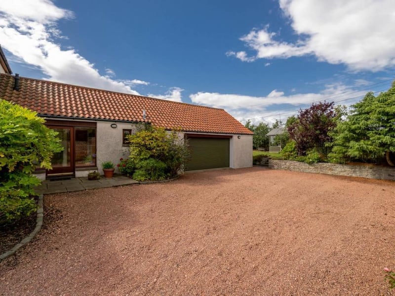 Gravelled parking area and double garage. The main door to the house can also be seen on the left.