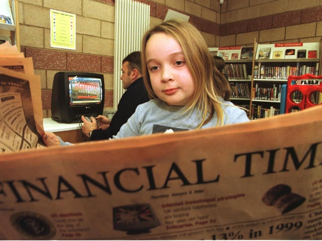 Sarah Mulligan, 8, from Colinton, reads the Financial times while Shaun Currie has a go on the new Playstation at the new Muirhouse Library, which was fully-equipped with internet ready computers with email(!), a Playstation and access to papers, magazines, videos and audio music, 6 January 2000.