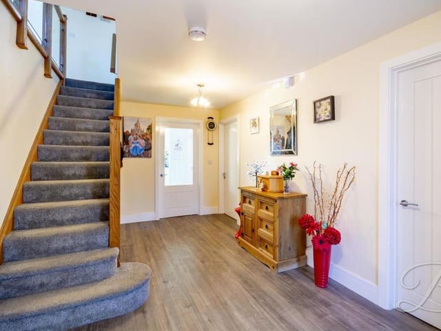 We're heading upstairs now, via this pleasant and welcoming hallway. It features laminate flooring and a wooden staircase with glass balustrade.