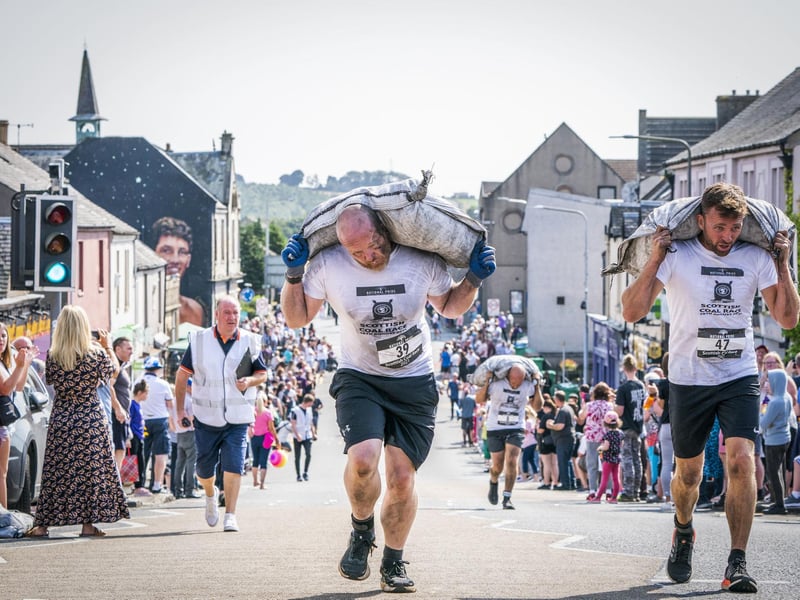 Competitors take part in the Scottish Coal Carrying Championships through the streets of Kelty in Fife. Picture date: Saturday August 28, 2021. PA Photo. The annual event is one of only two Coal Races in the world and the men's race requires participants to carry a 50-kilo bag of coal and the women's race requires a 25-kilo bag of coal to be carried over 1000 metres through the village. Photo credit should read: Jane Barlow/PA Wire