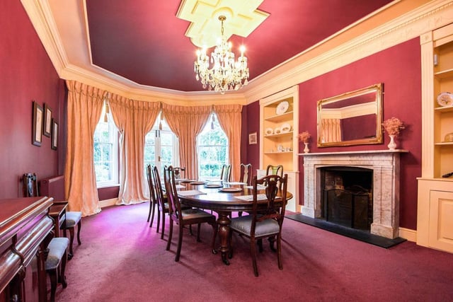 The luxurious formal dining room has a broad bay window, French doors and sash windows. There is a marble fireplace and built-in cupboards with shelving to either side of the chimney breast.