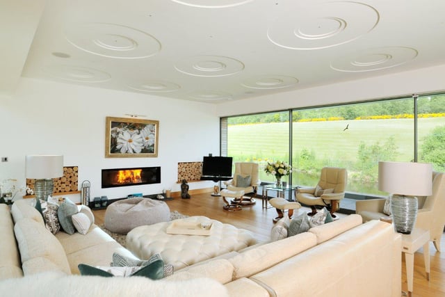 The modern living room is bathed in light from the large glass windows, and boasts an integrated fireplace and views overlooking the gardens.
