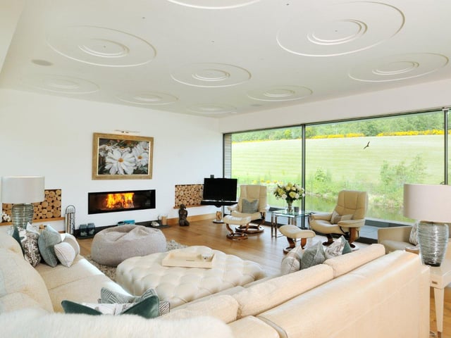 The modern living room is bathed in light from the large glass windows, and boasts an integrated fireplace and views overlooking the gardens.