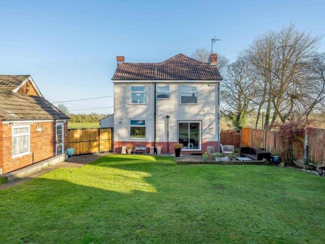 This shot shows the house standing tall, overlooking the lawn in the rear garden. A hard-standing path extends across the back of the property, leading to the garage and gates that provide access to the driveway.
