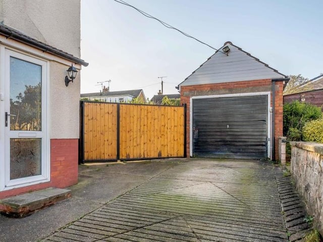 The long driveway, bordered by stone walls, that leads to the attached single garage. The large gates form the entrance to the back garden.