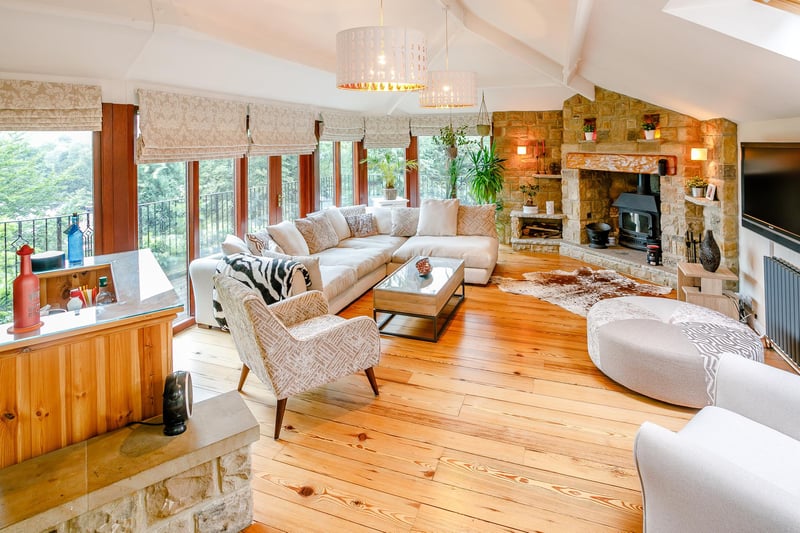 Spacious, dual-aspect sitting room, displaying a full elevation-of-floor to ceiling glazing which hold double doors out to a second balcony area, in addition to original wood flooring, vaulted ceilings, a bar area and an exposed stone fireplace with inset log burner.