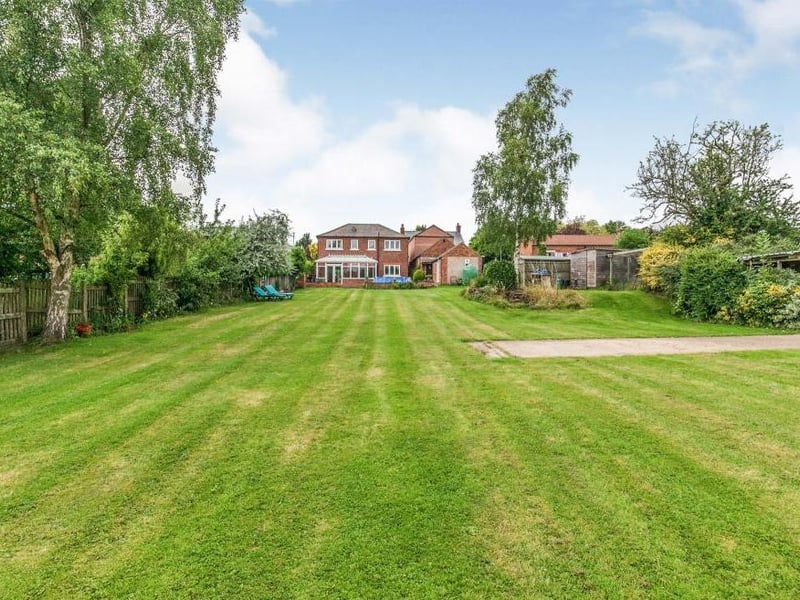 The back garden, which is mainly laid to lawn. It also has patio areas, lighting, a tap, a pond and smaller sheds.