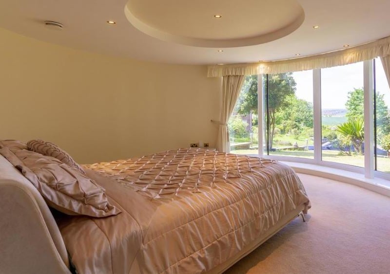The main bedroom with a panoramic, curved window looking out on to the front of the property. There are also patio doors leading outside.