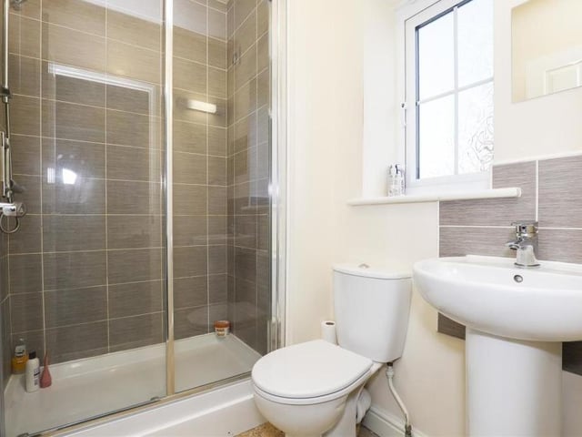 The en suite to the master bedroom features a shower enclosure with a wall-mounted shower, a low-level flush WC and a pedestal wash basin. The floor is tiled, as are some of the walls, while there is also a wall-mounted radiator, an extractor fan and a uPVC double-glazed, opaque window to the back.