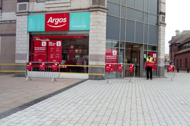 A member of staff waits outside Argos with safety barriers in place for customers to queue.