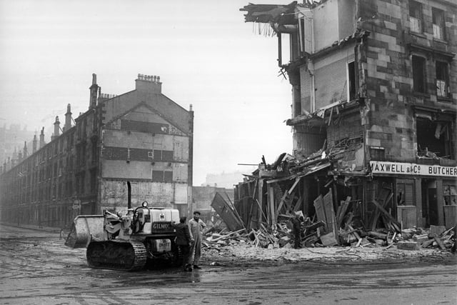 1960:  Workmen and a bulldozer beside a tenement being demolished.