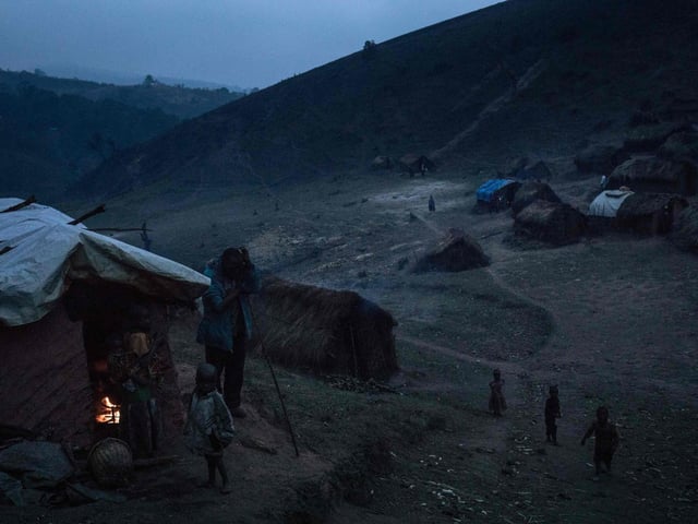 Displaced persons from the Bafuliru community stand amidst the makeshift shelters of the internally displaced persons camp of Bijombo.