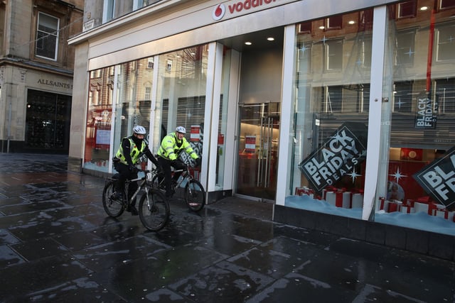 Police officers on cycles pass a Vodafone store on a quiet Buchanan Street in Glasgow.