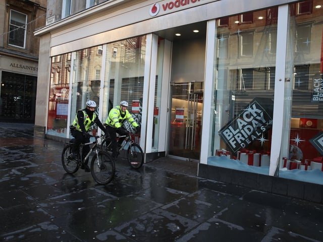 Police officers on cycles pass a Vodafone store on a quiet Buchanan Street in Glasgow.