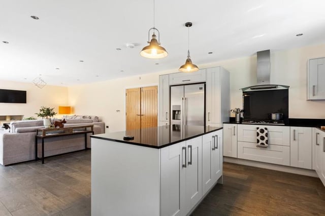 The open plan area is the perfect space for cooking, entertaining and relaxing. Appliances include a double eye-level oven, five-ring gas hob, extractor fan, American fridge freezer and integrated dishwasher. In the background, you can see the living room, while there are also bi-fold doors giving access to the garden.