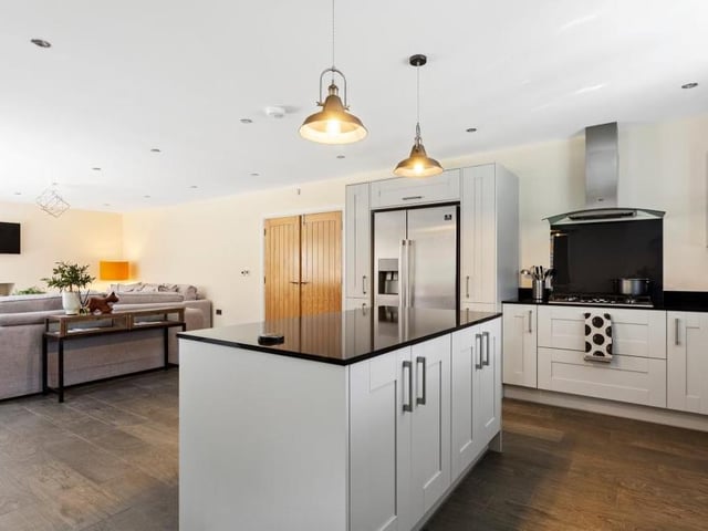 The open plan area is the perfect space for cooking, entertaining and relaxing. Appliances include a double eye-level oven, five-ring gas hob, extractor fan, American fridge freezer and integrated dishwasher. In the background, you can see the living room, while there are also bi-fold doors giving access to the garden.