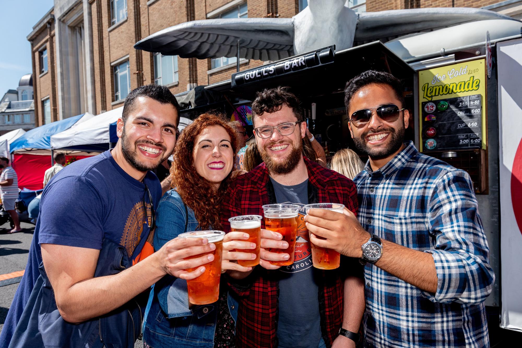 Southsea Food Festival 2019 at Palmerston Road, Southsea - Akshaya Chapagain, Marta Gallego, Edward Fraser and Rajeev Bhandari says cheers with their Hop House 13lager. All were students at University of Portsmouth five years ago and came back to Portsmouth to see each other and the city again. Picture: Vernon Nash 200719-015