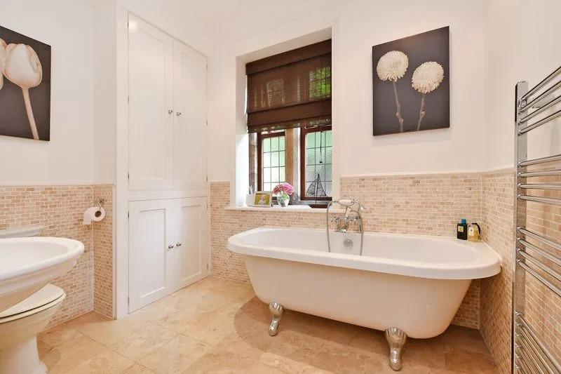 The bathroom has a white suite with a clawed feet bath, a shower attachment, a wash basin, WC, and sympathetic tiling, including underfloor heating.