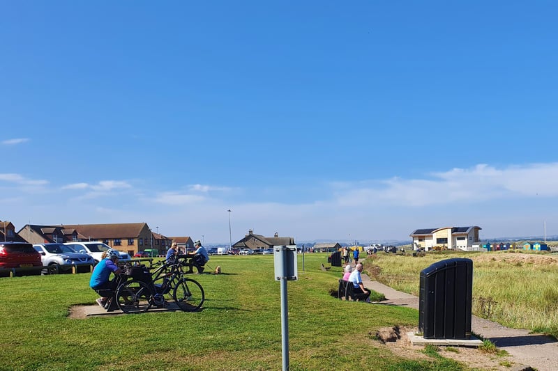 Cyclists, tourists and residents enjoy sitting on benches, cycling by the beach and generally relaxing while enjoying the weather.