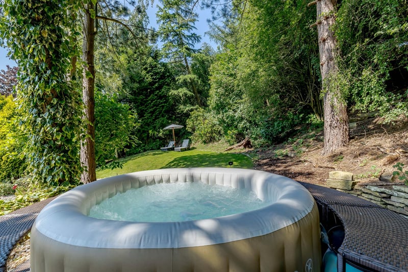 Steps lead onto a lawned area which is bound by mature trees and shrubbery with a pathway winding up to a small wooded area and onto the hot tub platform.