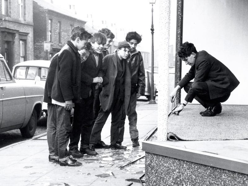 Youngsters watch as John Townend starts to clear up the wrecked window of Peter Pell's shop at Atterclife after the hurricane in Sheffield in February 1962
