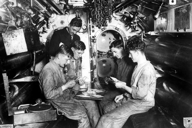 circa 1942:  Crew of a submarine docked in Portsmouth having a game of cards while listening to a gramophone record in the torpedo firing room.  (Photo by Keystone/Getty Images)