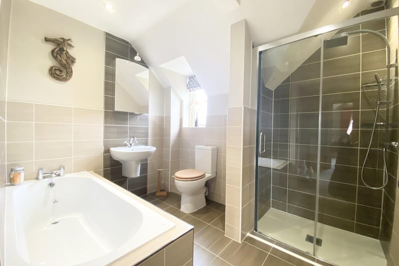 Four-piece suite comprising double shower cubical with rainfall showerhead and a hand shower attachment, glass door front, modern pedestal wash hand basin with mixer tap, low-level flush WC, recessed bath with mixer taps and a tiled font panel finished with chrome effect beading.