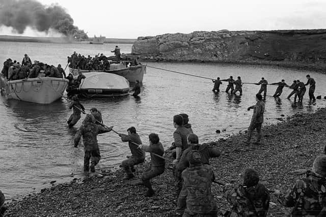 Survivors from HMS Sir Galahad (ablaze in the background) are hauled ashore by colleagues at Bluff Cove, East Falkland, after the ship was hit by an Argentinian air attack on June 29, 1982, during the Falklands conflict.