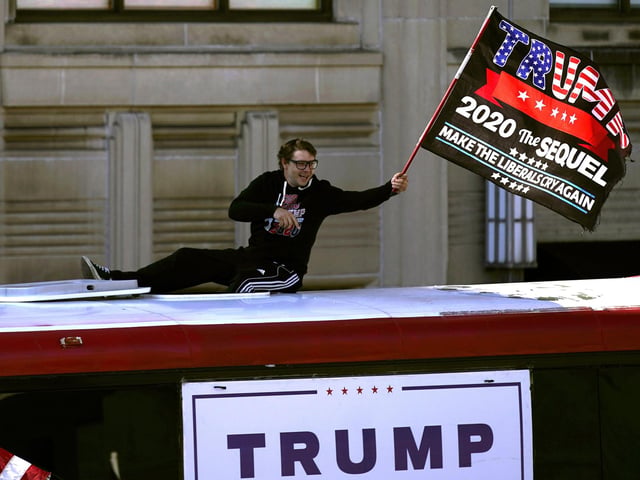 A supporter of President Donald Trump waves a flag from atop a bus outside the Pennsylvania State Capitol. (AP Photo/Julio Cortez)