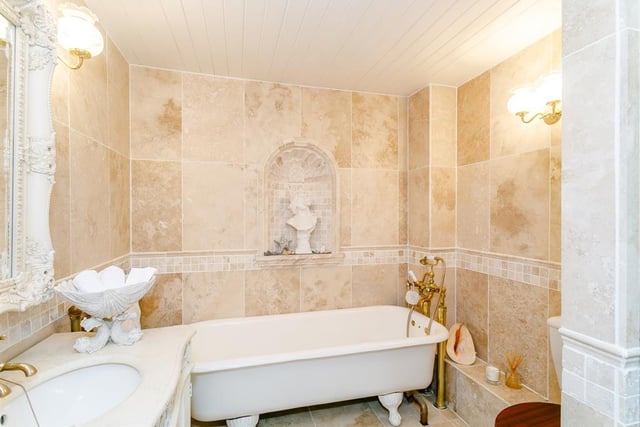 The fully tiled bathroom has a decorative Roman-style arched alcove, a free-standing roll top bath, separate shower cubicle and a brass wall-mounted heated towel rail.