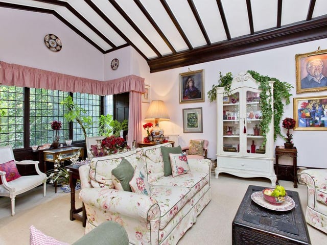 The impressive drawing room has a vaulted ceiling with exposed beams and large glass box bay windows.