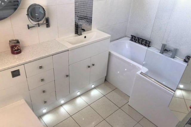 The house has two bathrooms - this one is a fully tiled, white, three piece bathroom suite that includes the toilet, bath, glass shower screen, hand wash basin and vanity unit