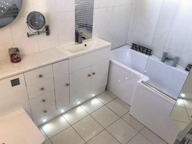 The house has two bathrooms - this one is a fully tiled, white, three piece bathroom suite that includes the toilet, bath, glass shower screen, hand wash basin and vanity unit