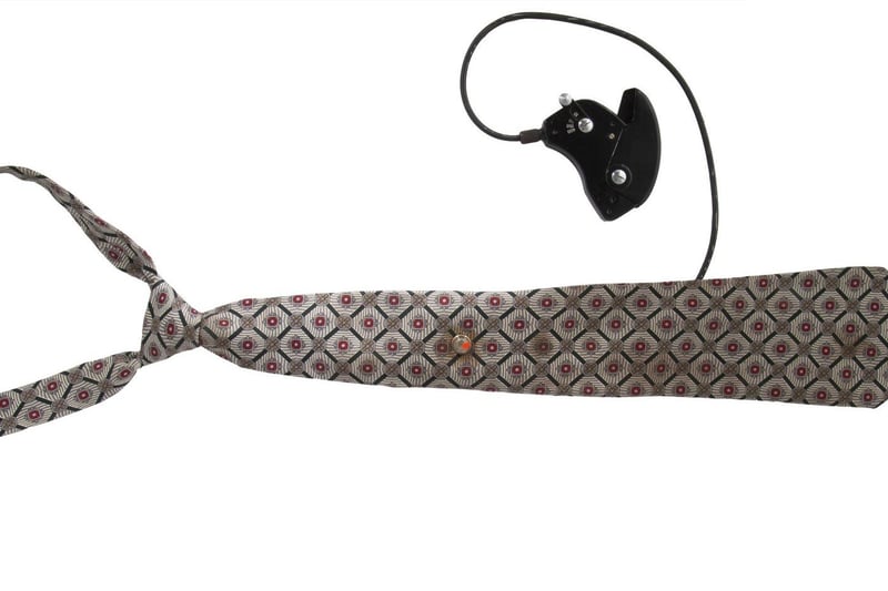 A Soviet KGB spy silk necktie with a hidden "Tochka-58" camera concealed with use of a fake tie clip. Includes hand activated shutter release mechanism. Also includes a reproduction photograph of a similar tie and how it was to be worn, as well as an additional regular tie clip and a fake tie clip with camera lens. Estimate: $2,000-$3,000.
