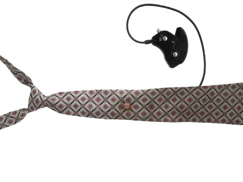A Soviet KGB spy silk necktie with a hidden "Tochka-58" camera concealed with use of a fake tie clip. Includes hand activated shutter release mechanism. Also includes a reproduction photograph of a similar tie and how it was to be worn, as well as an additional regular tie clip and a fake tie clip with camera lens. Estimate: $2,000-$3,000.