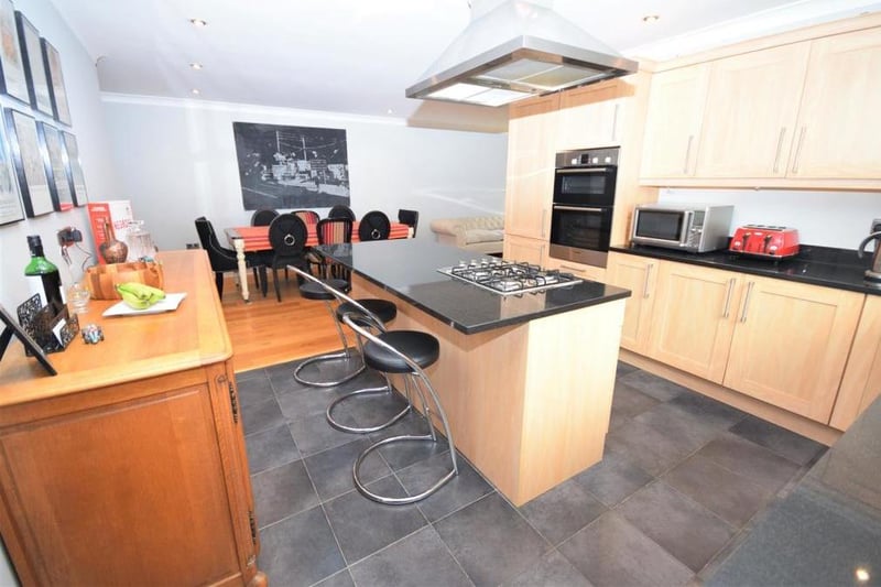 Another view of the kitchen, which has a modern., sociable feel. It is fitted with a range of wall and base units, and boasts a double oven and a breakfast-island inset with a four-ring gas hob and extractor over.