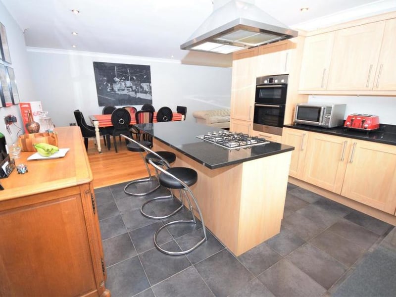 Another view of the kitchen, which has a modern., sociable feel. It is fitted with a range of wall and base units, and boasts a double oven and a breakfast-island inset with a four-ring gas hob and extractor over.