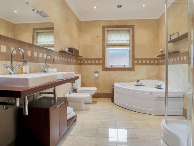 This luxurious en suite to the master bedroom features his and hers sinks, a close-coupled WC, bidet, corner jacuzzi-style bath and double-width shower cubicle with spa shower fittings. It is fully tiled, with ceiling spotlights and vanity-unit storage.
