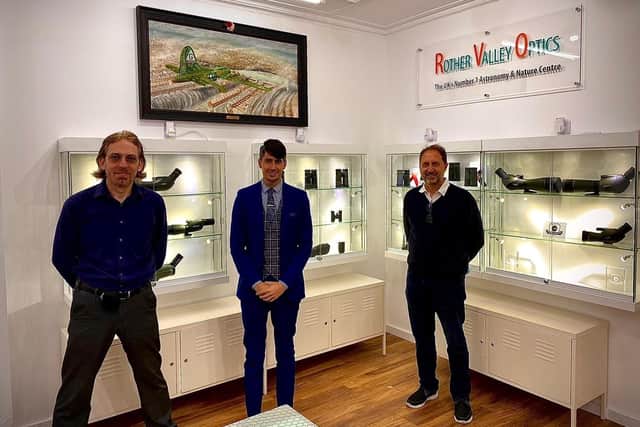 The original oil painting depicting the last moments of the stricken USAF B17 bomber ’Mi-Amigo’ being proudly displayed in its new home at Rother Valley Optics. Left to right: Ian Littlewood, owner of Rother Valley Optics, Adam Khatib, Shop Manager and artist, Paul Rowland.

