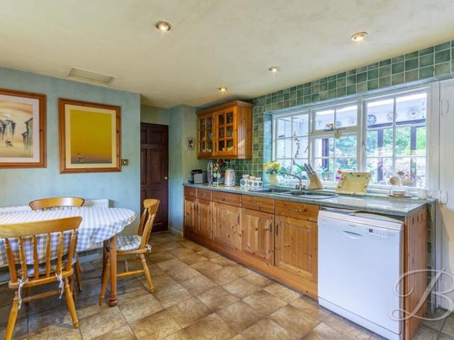 Another view of the kitchen, which has a large window overlooking the garden. An inset sink and drainer has a mixer tap above, while the floor is tiled.