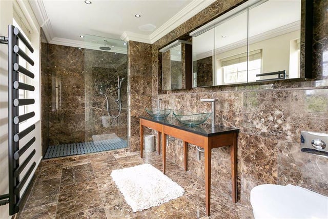 The property features four bathrooms throughout, including this luxurious shower room, complete with marble effect tiling, double sink, and mirror storage units.