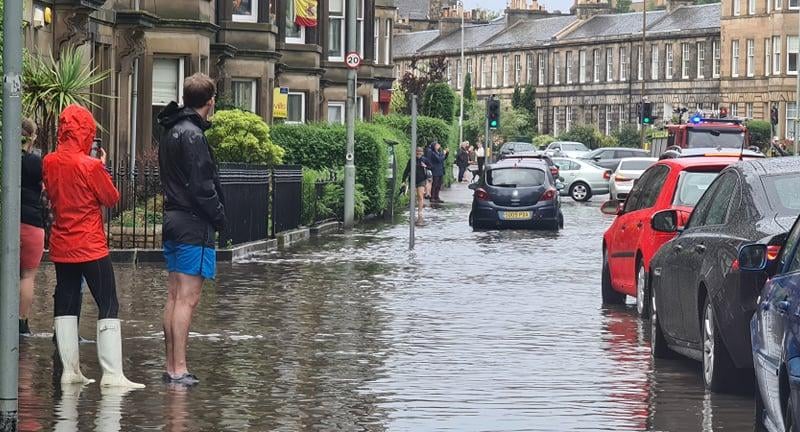 Pedestrians in Stockbridge with their hoods up as heavy rainfall floods streets in Edinburgh's New Town.