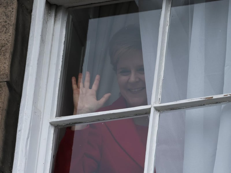 Nicola Sturgeon waves from a window, after holding a press conference, as people gather outside of Bute House. Picture: Jeff J Mitchell/Getty Images