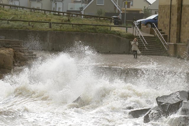 A woman watches on as strong waves splash onto the shore.