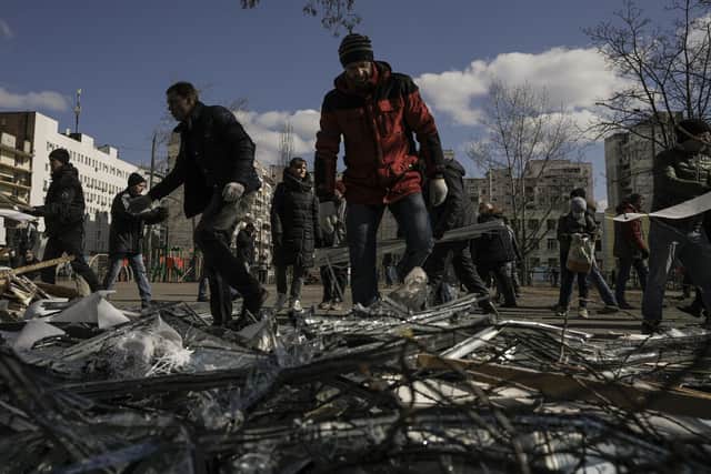 People clear debris outside a medical center damaged after parts of a Russian missile, shot down by Ukrainian air defense, landed on a nearby apartment block, according to authorities, in Kyiv, Ukraine, Thursday, March 17, 2022. Russian forces destroyed a theater in Mariupol where hundreds of people were sheltering Wednesday and rained fire on other cities, Ukrainian authorities said, even as the two sides projected optimism over efforts to negotiate an end to the fighting. (AP Photo/Vadim Ghirda)