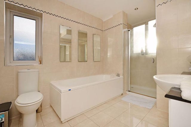 The main bathroom has a walk-in shower with glass door, a double ended bath, a sink with vanity unit below, WC and chrome towel radiator with cream floor and wall tiles.