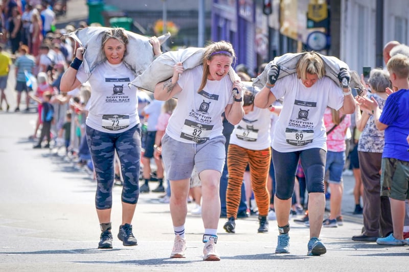 Competitors in the Women's Race take part in the Scottish Coal Carrying Championships through the streets of Kelty in Fife.  Picture date: Saturday August 28, 2021. PA Photo. The annual event is one of only two Coal Races in the world and the men's race requires participants to carry a 50-kilo bag of coal and the women's race requires a 25-kilo bag of coal to be carried over 1000 metres through the village. Photo credit should read: Jane Barlow/PA Wire 