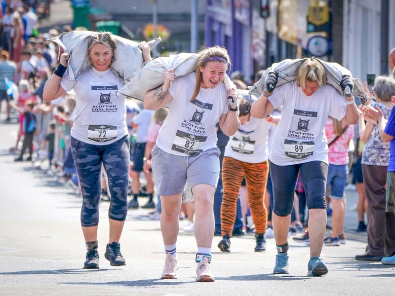 Competitors in the Women's Race take part in the Scottish Coal Carrying Championships through the streets of Kelty in Fife. Picture date: Saturday August 28, 2021. PA Photo. The annual event is one of only two Coal Races in the world and the men's race requires participants to carry a 50-kilo bag of coal and the women's race requires a 25-kilo bag of coal to be carried over 1000 metres through the village. Photo credit should read: Jane Barlow/PA Wire