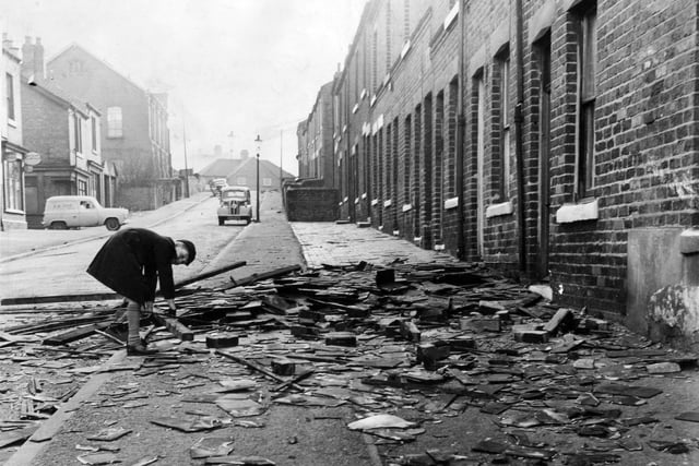 An inquisitive school boy bends to get a closer look at the wreckage of roof slates and wood strewn over the pavement of School Street, Rotherham, after the hurricane in February 1962