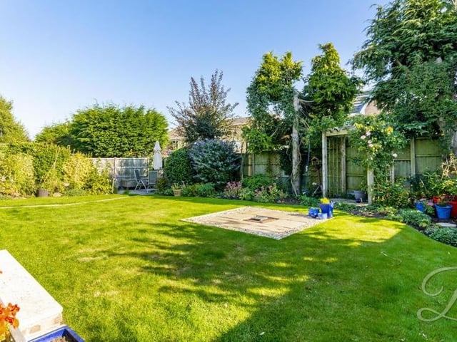 Another view of the back garden, which shows it offers colour and privacy. The lawn is surrounded by planted borders and a fence.